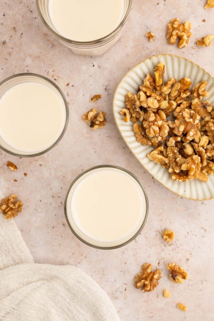 An overhead shot of three glasses of homemade walnut milk with a bowl of walnuts on the side.