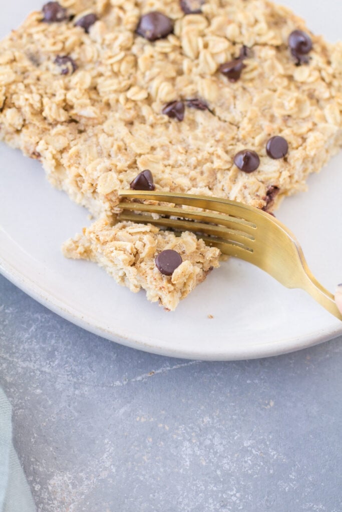 A gold fork taking a bite out of chocolate peanut butter oatmeal on a white plate