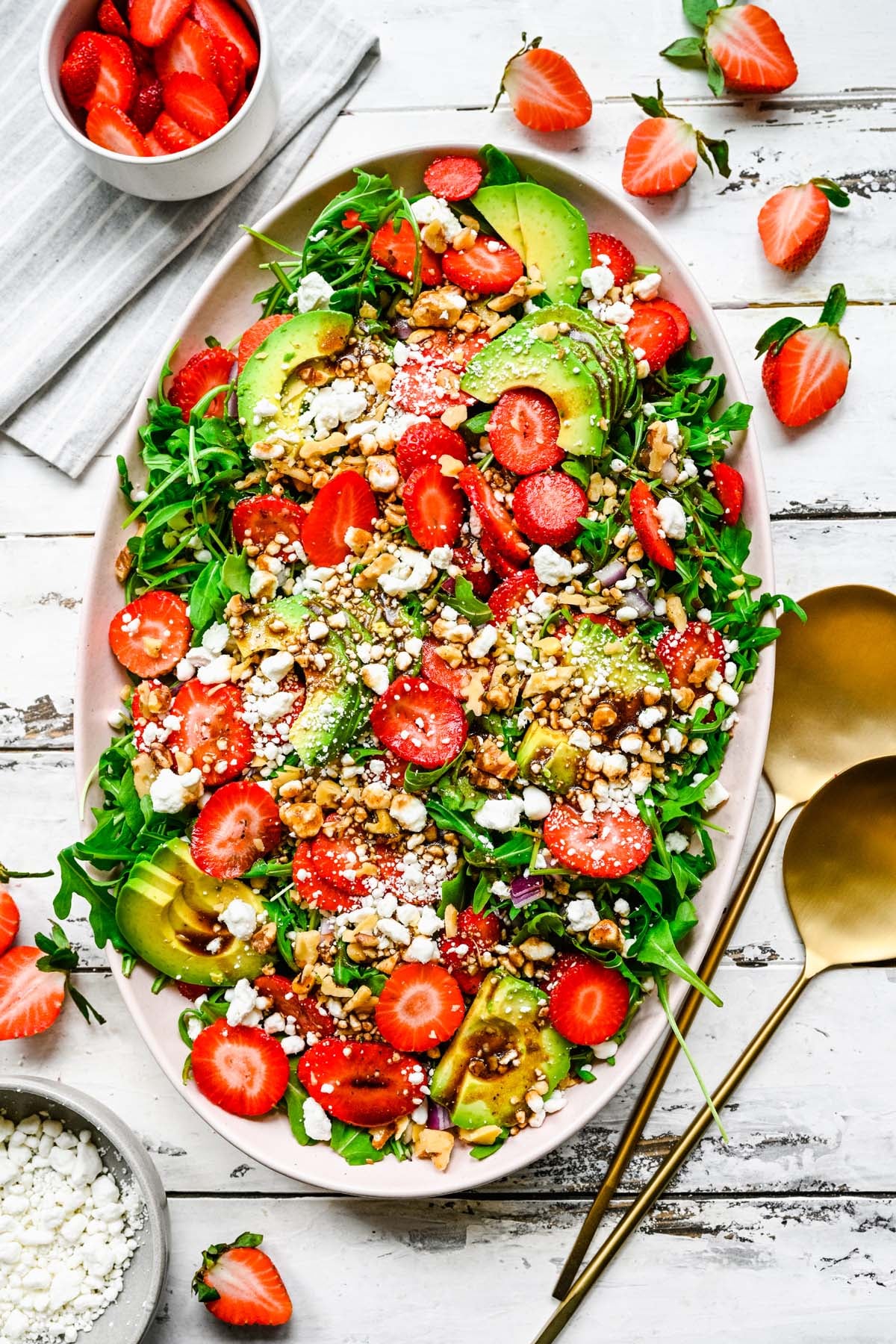 A large white bowl with strawberry goat cheese salad on a white background with more strawberries on the side