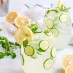 Cucumber drink with vodka on a white background. Two cocktails with lemons, cucumbers and mint garnishing them.