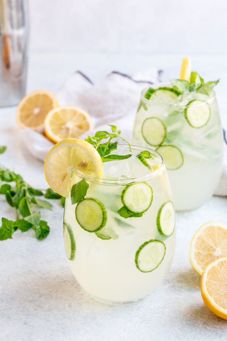 Cucumber drink with vodka on a white background. Two cocktails with lemons, cucumbers and mint garnishing them.