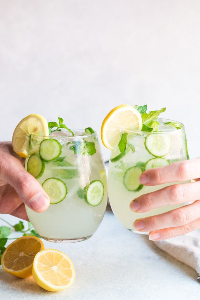 Two hands cheers-ing a cucumber cocktail. A light, refreshing drink