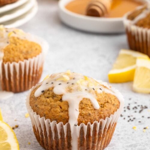 Healthy Lemon Chia Seed Muffin topped with a glaze with more muffins and lemon slices in the background.