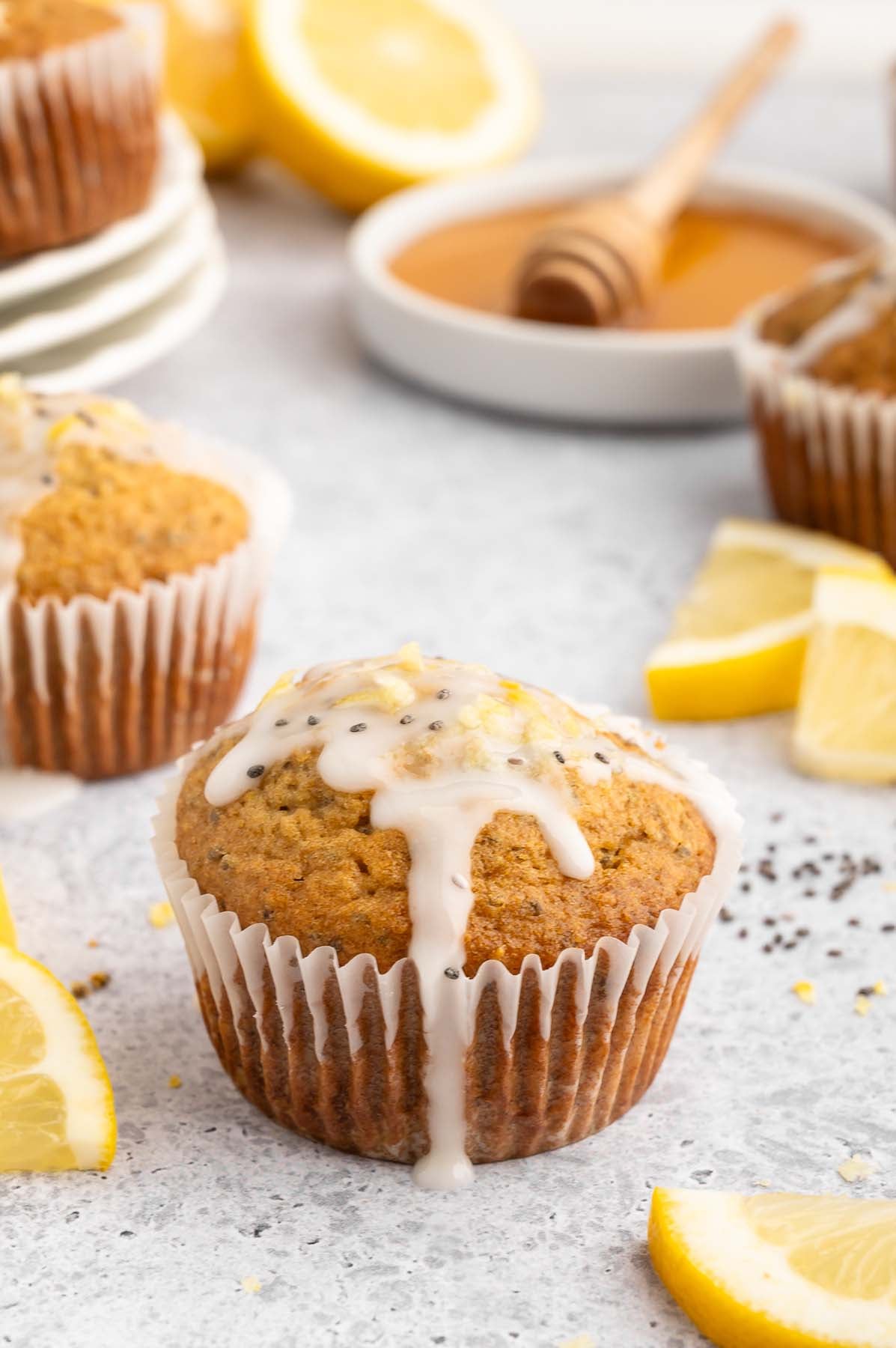 Homemade lemon chia seed muffin topped with glaze and extra chia seeds. More muffins and lemon slices sit in the background.