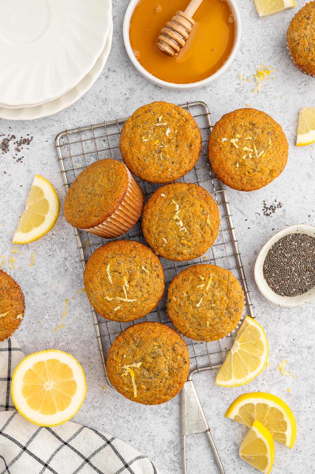 Overhead view of gluten free lemon muffins on a wire cooling rack surrounded by fresh lemon slices and a small container of honey.