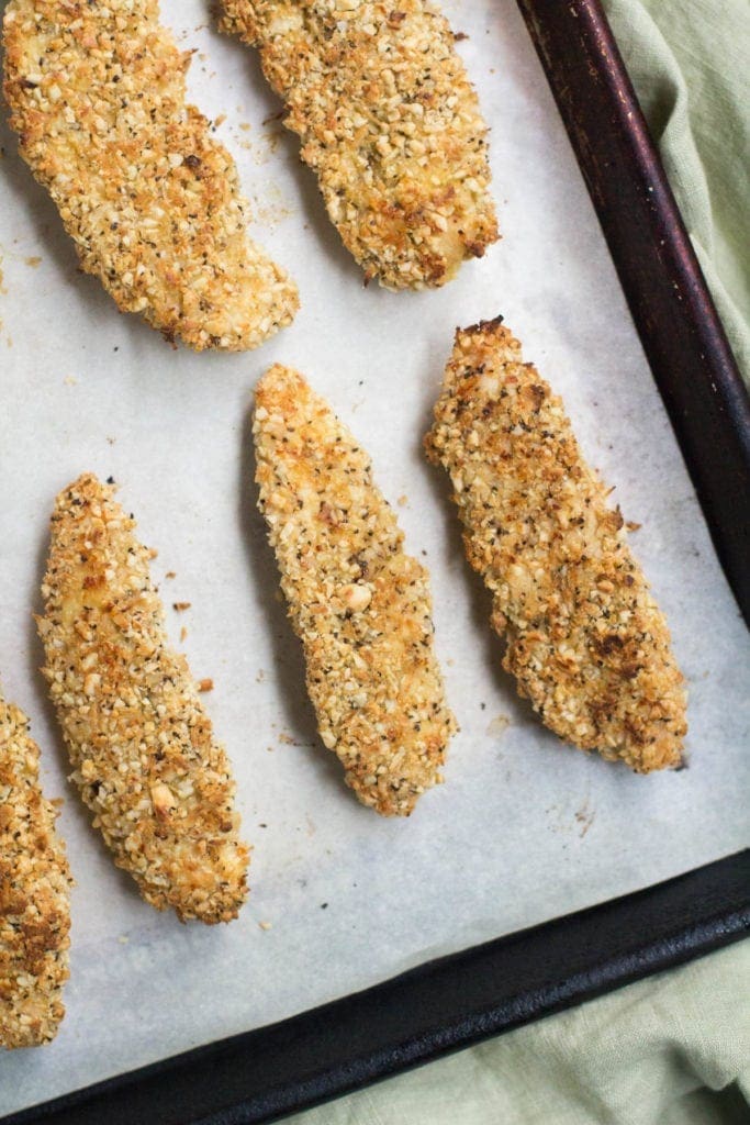 Chicken tenders on a baking sheet lined with parchment paper that have just come out of the oven.