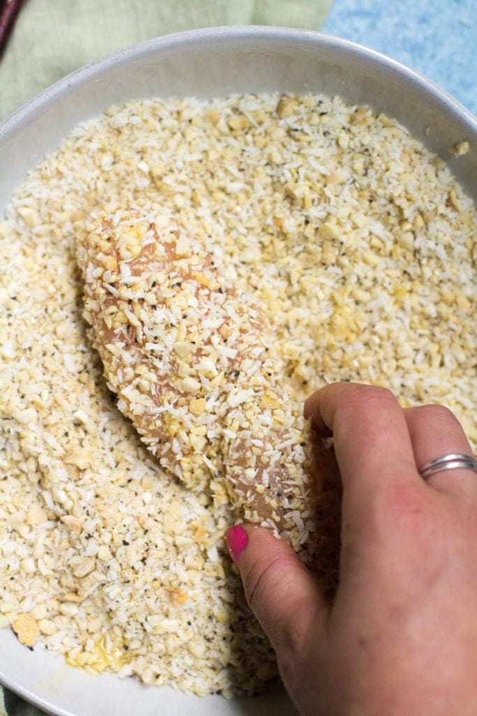 Whole30 Cashew Coconut Chicken Tenders being dipped in a bowl of coconut cashew batter