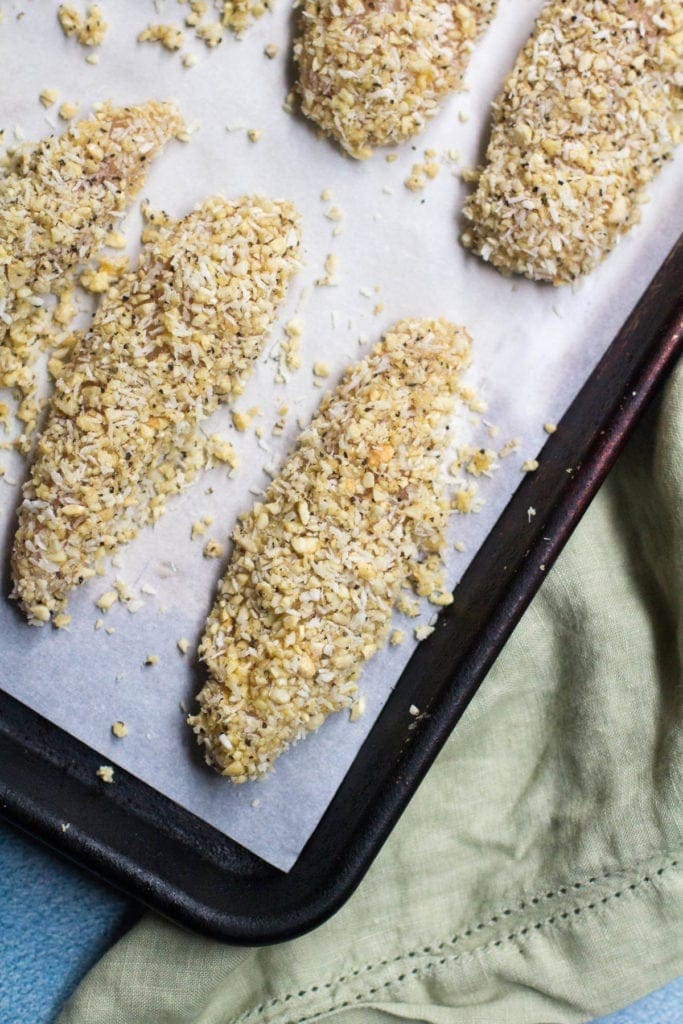 Whole30 Cashew Coconut Chicken Tenders laid out on a parchment lined baking sheet ready to go in the oven.