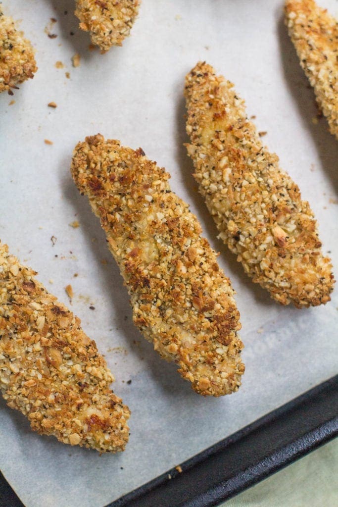 Golden brown Whole30 Cashew Coconut Chicken Tenders fresh out of the oven on a parchment lined baking sheet.