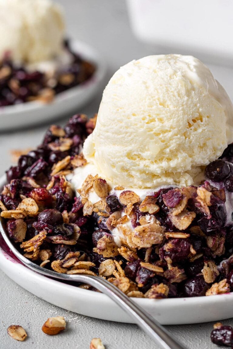 Healthy Blueberry Crisp on a white dish with a scoop of vanilla ice cream
