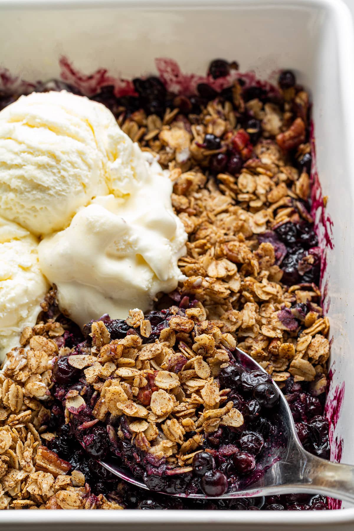 Gluten Free Blueberry Crisp in a white dish with a spoon scooping some out.