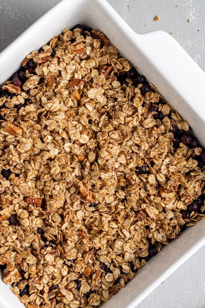 A close up of healthy blueberry crisp in a white baking dish on a grey background