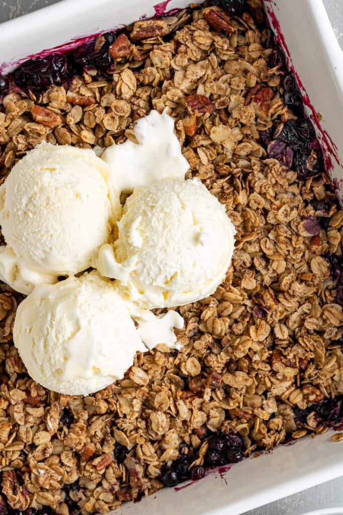 Healthy Blueberry Crisp in a white dish with vanilla ice cream on top.