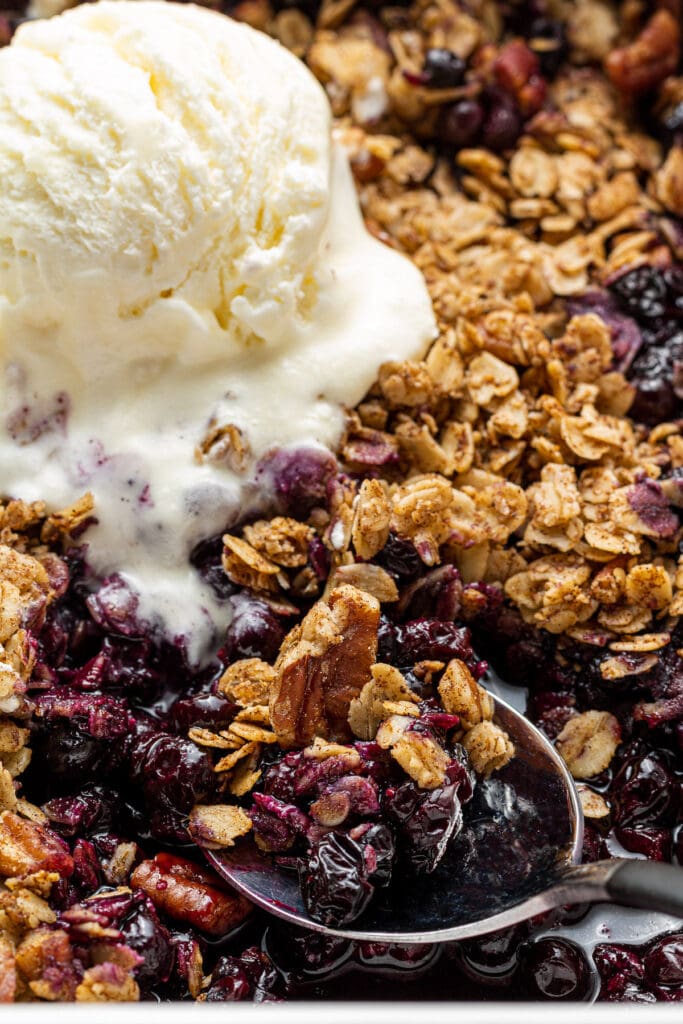 A close up of blueberry crisp with a spoon scooping out of the dish