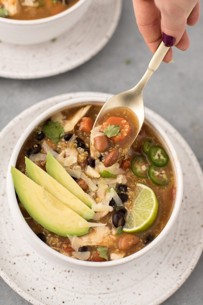 A bowl of quinoa taco soup with a gold spoon taking a bite out of it.