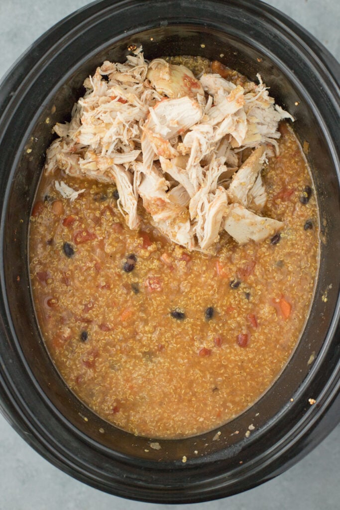 An overhead shot of shredded chicken being added to a crockpot