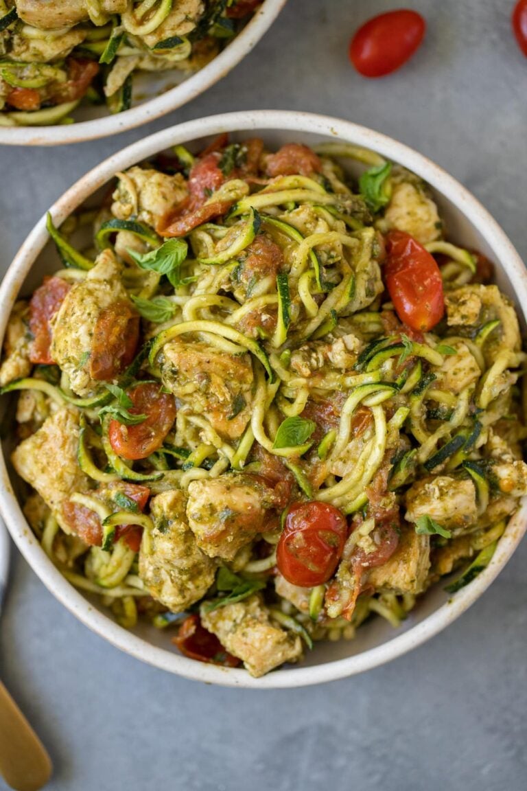 Whole30 Pesto Chicken Zucchini Noodles in a white bowl with tomatoes and basil scattered around.