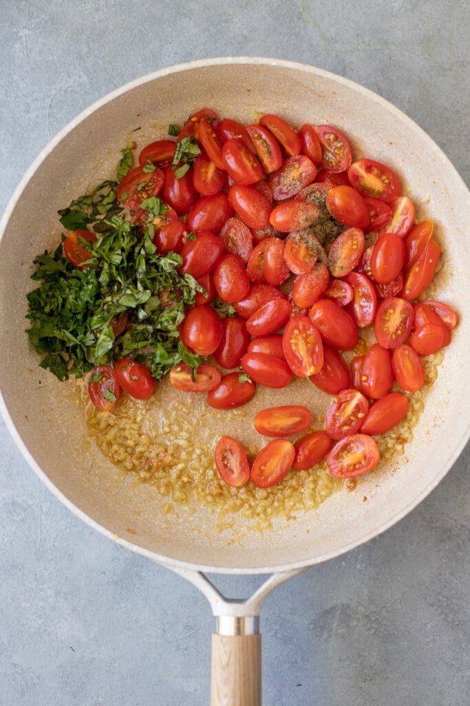 Tomatoes, fresh herbs and garlic in a pan for pesto chicken pasta