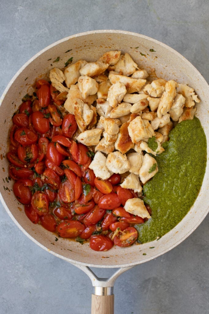 Sauted tomatoes, pesto and chicken breasts in a pan on a grey background for pesto chicken zoodles