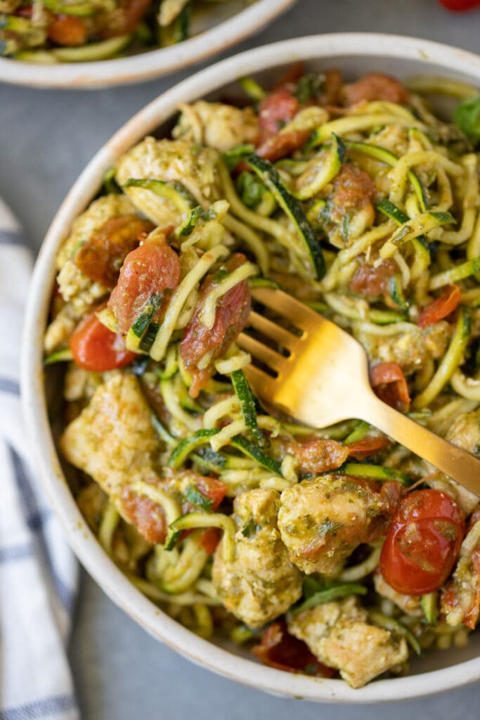 A gold fork with zoodles wrapped around it on top of Easy Whole30 Pesto Chicken Zoodles