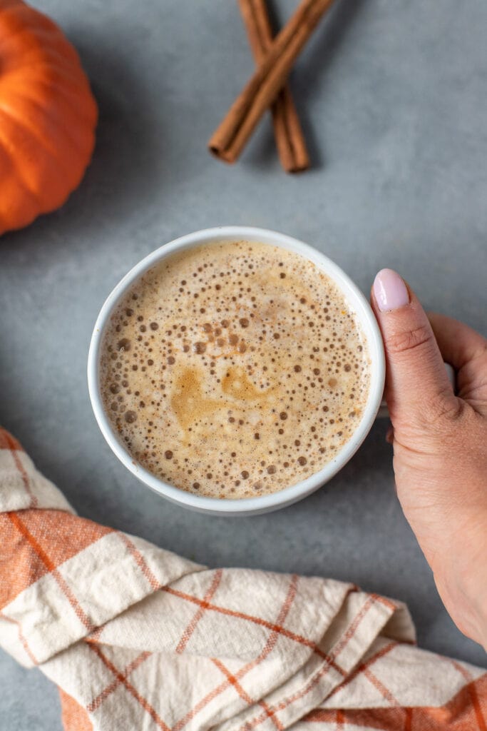 Easy Homemade Pumpkin Spice latte on a grey background with an orange plaid linen and small pumpkin