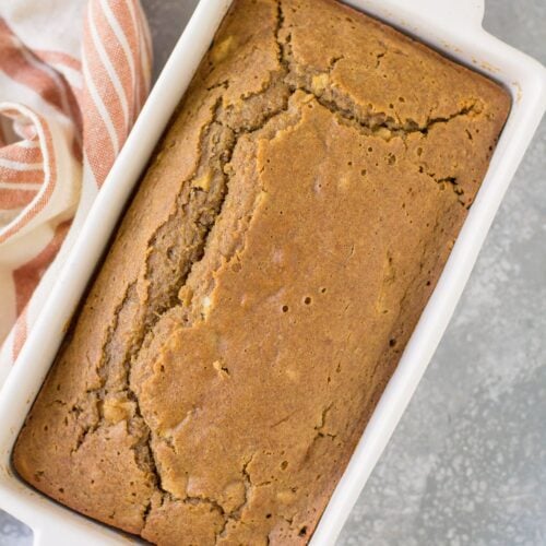 Apple cider bread in a white baking loaf pan on a grey background
