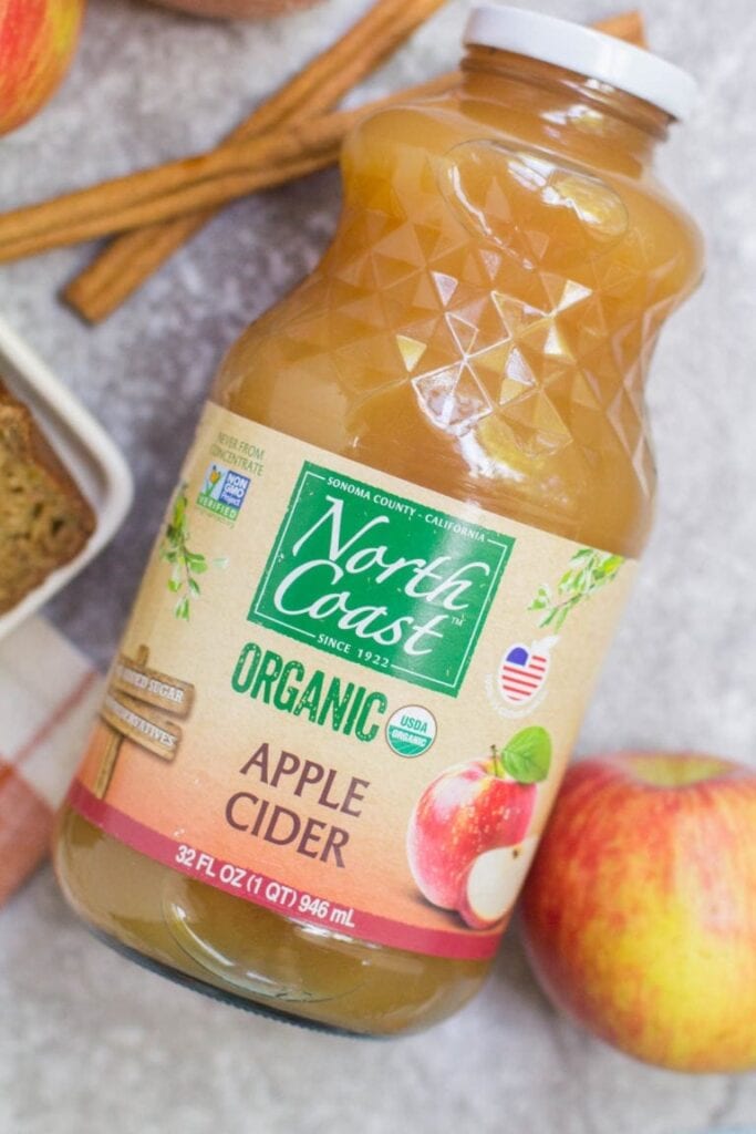 Apple cider with ingredients for bread scattered around it.
