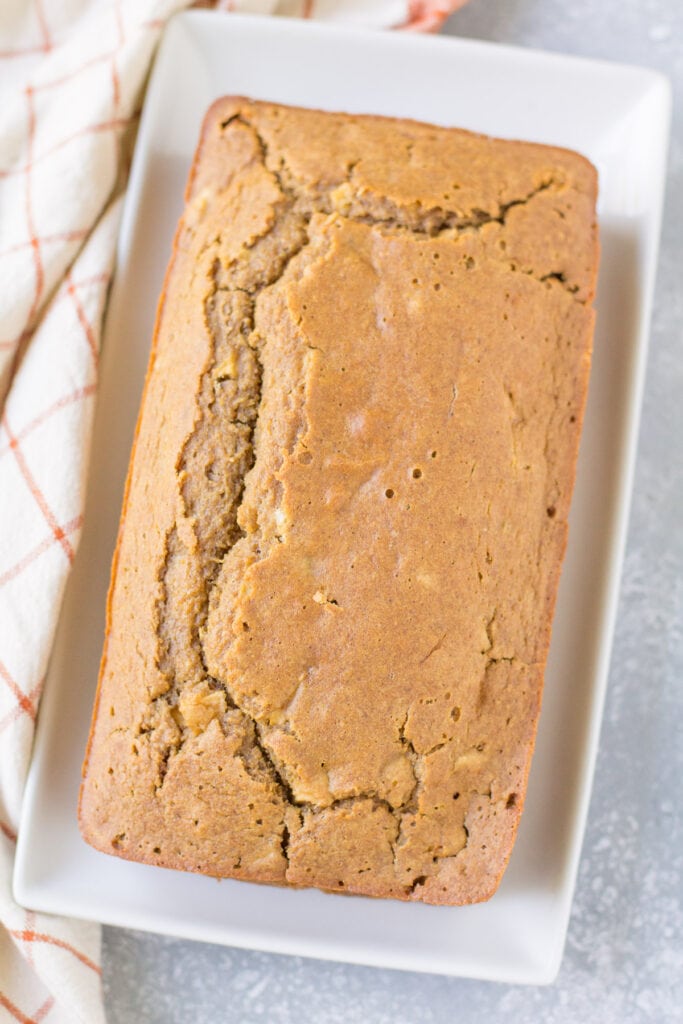 An overhead shot of apple cider bread on a white plate with red plaid linen to the left
