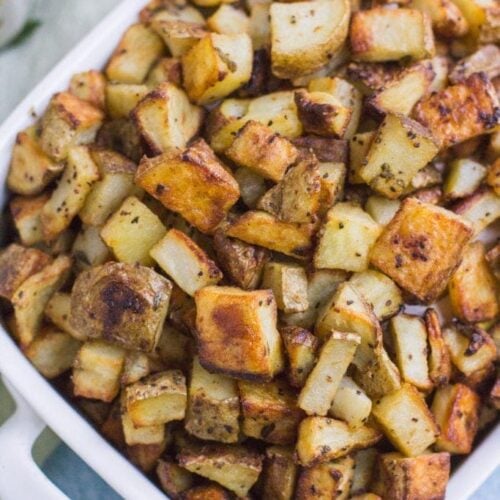 Crispy Dijon Roasted Potatoes in a white bowl on a blue background.