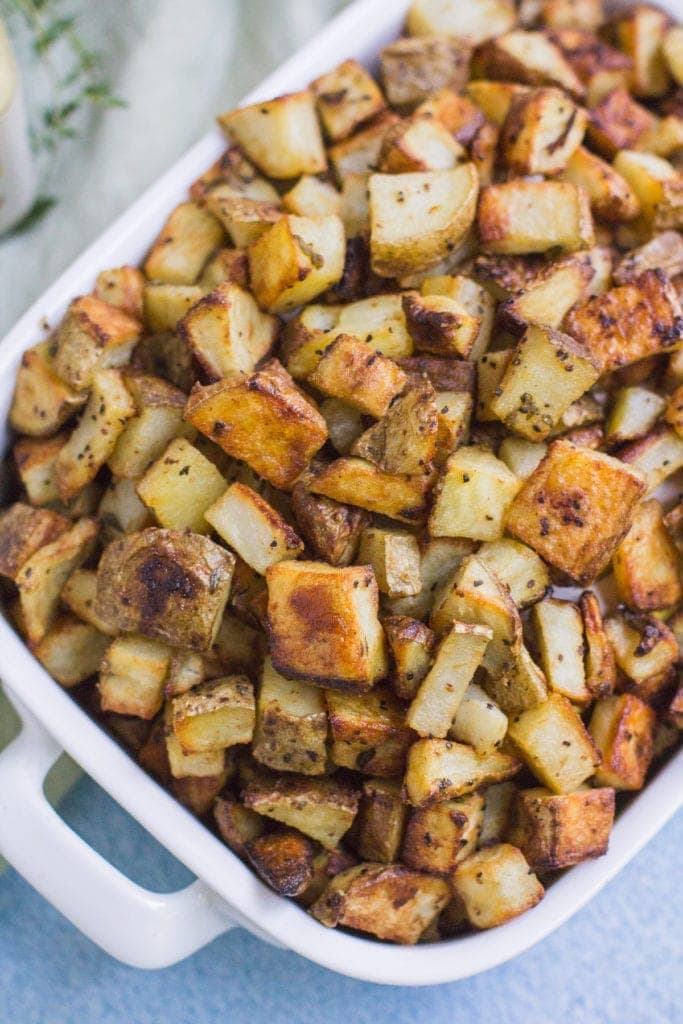 Crispy Dijon Roasted Potatoes in a white bowl on a blue background.