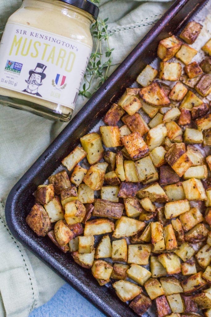 Easy Crispy Dijon Roasted Potatoes on a sheet pan with a green linen and Sir Kensinton's mustard off to the side.