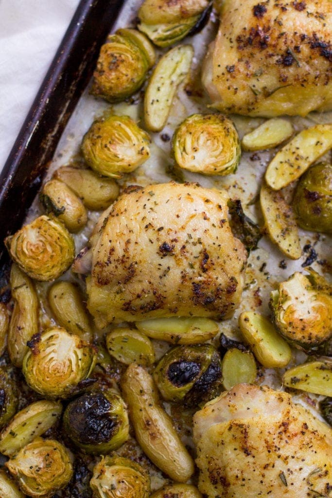 Lemon Rosemary Chicken Thighs, potatoes and brussels sprout on a parchment lined sheet pan.