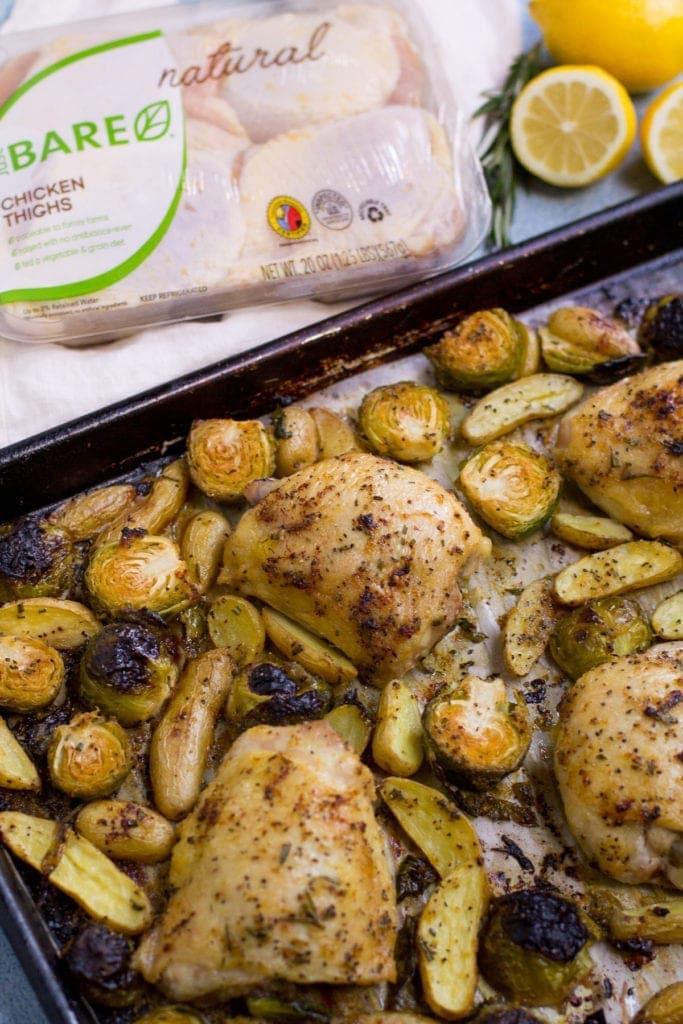 Sheet Pan Lemon Rosemary Chicken Thigh Dinner coming out of the oven on a black baking sheet with a package of Just BARE chicken off to the side.