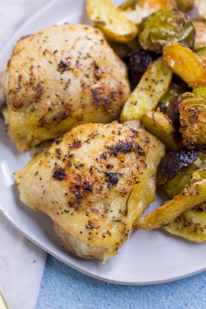 Sheet Pan Lemon Rosemary Chicken Thigh Dinner on a white plate out of the oven. Close up image of the crispy chicken thighs.