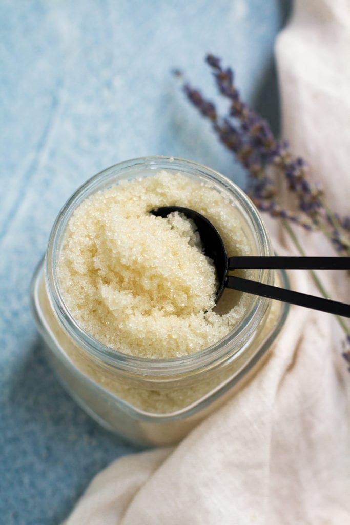 Homemade sugar scrub in a glass jar with a scooper coming out of it.