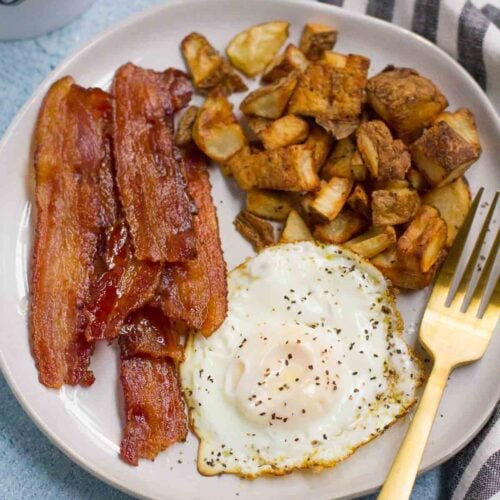 How to Cook Crispy Bacon - showing bacon on white plate with potatoes and a fried egg.
