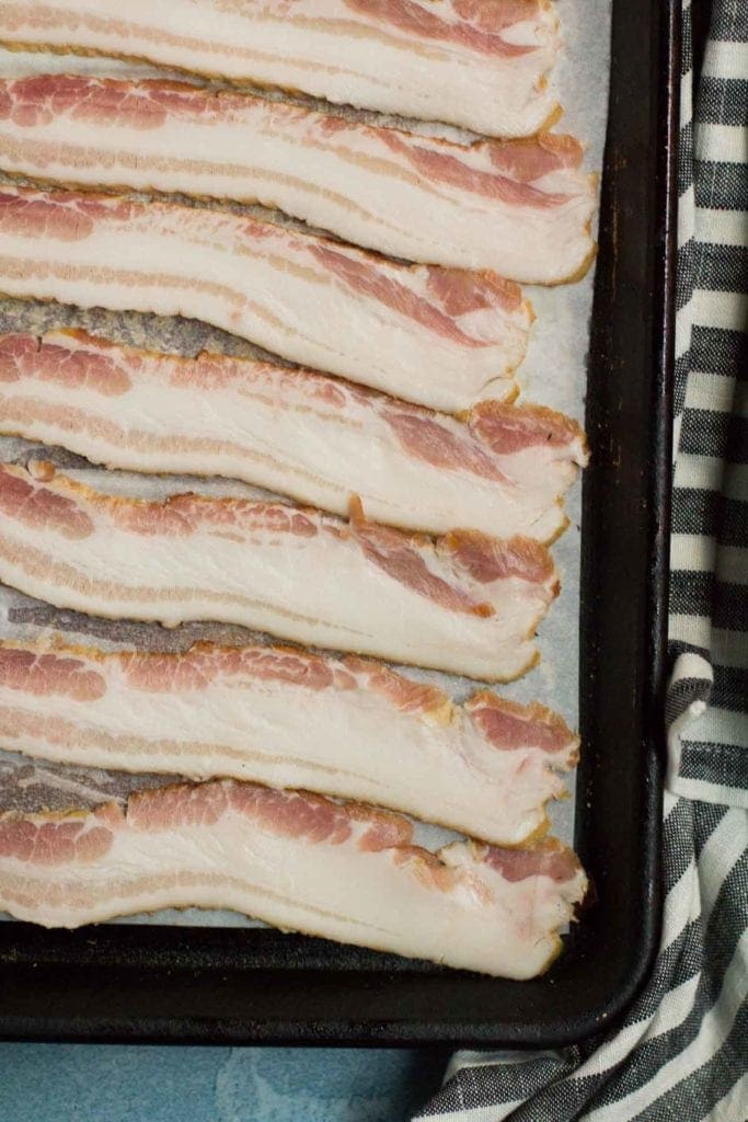 Raw bacon on a parchment paper lined baking sheet getting ready to be turned into crispy bacon.