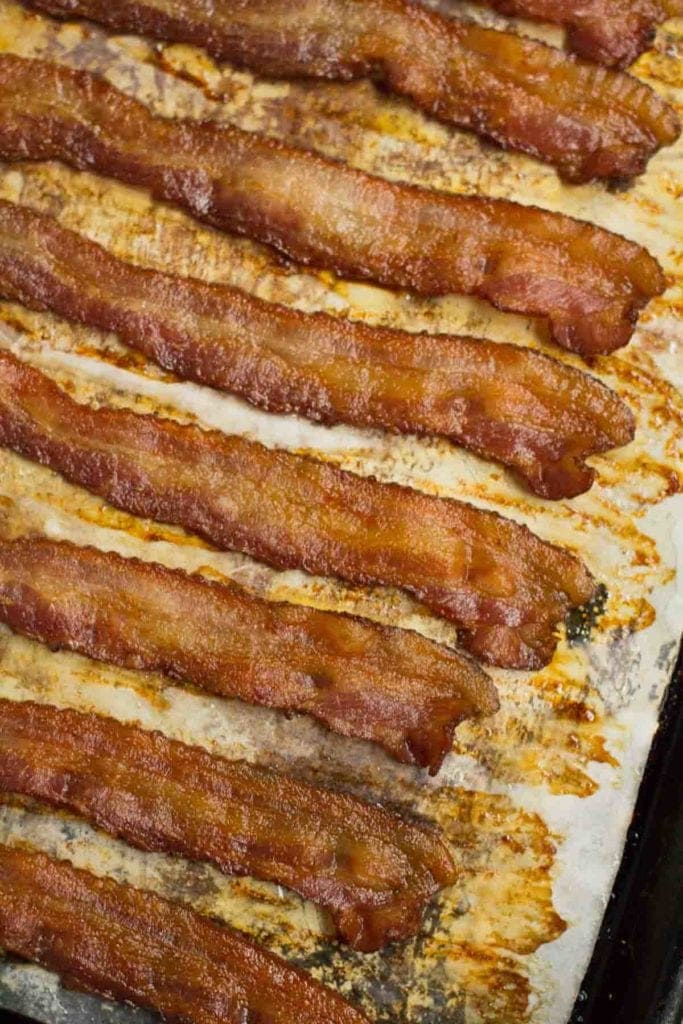 Crispy bacon on a parchment paper lined baking sheet coming out of the oven.