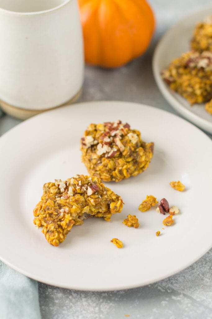 Pumpkin Breakfast Cookies on a white plate with a cup of coffee, pumpkin, and plate of cookies in the background.