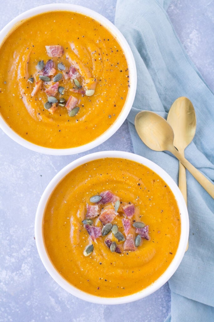 Two bowls of easy butternut squash soup on a grey background with spoon and blue linens off to the side.