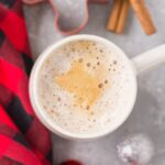 An overhead shot of a healthy gingerbread latte on a grey background with a red checked linen, ornaments and cinnamon sticks off to the side.