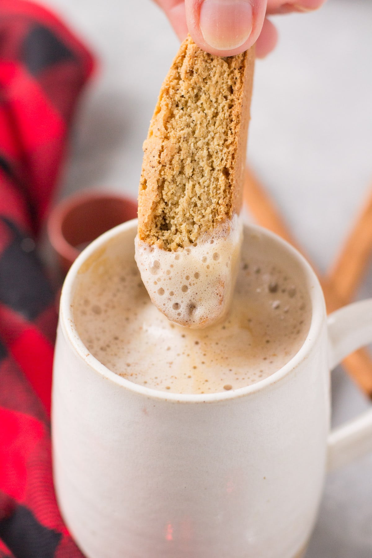 A biscotti being dipped into a white mug filled with a healthy gingerbread latte