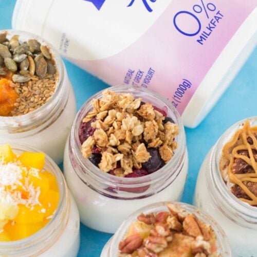 5 Healthy Yogurt Parfaits in glass jars with a carton ofFAGE Yogurt off to the side