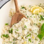A pan full of healthy lemon basil risotto with a wooden spoon taking out a serving.