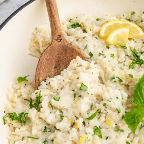 A pan full of healthy lemon basil risotto with a wooden spoon taking out a serving.