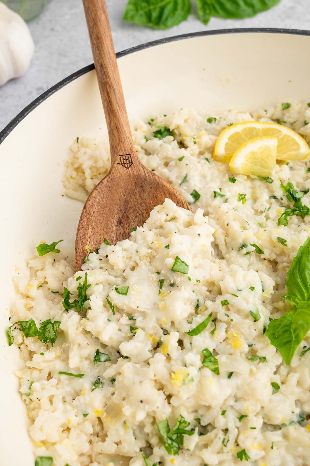 A pan full of lemon risotto and a wooden spoon removing a serving.