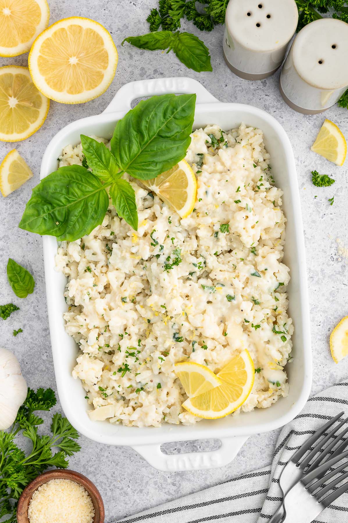 A white serving dish of lemon rice garnished with a sprig of basil and lemon slices.