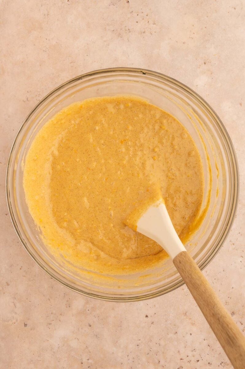 Batter for orange muffins in a clear bowl with a rubber spatula in it.