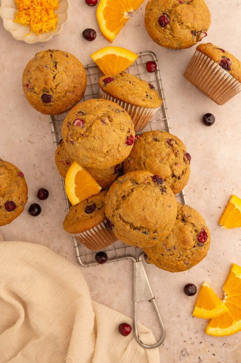 Cranberry Orange Muffins piled on a wire rack with fresh cranberries and orange slices around it.