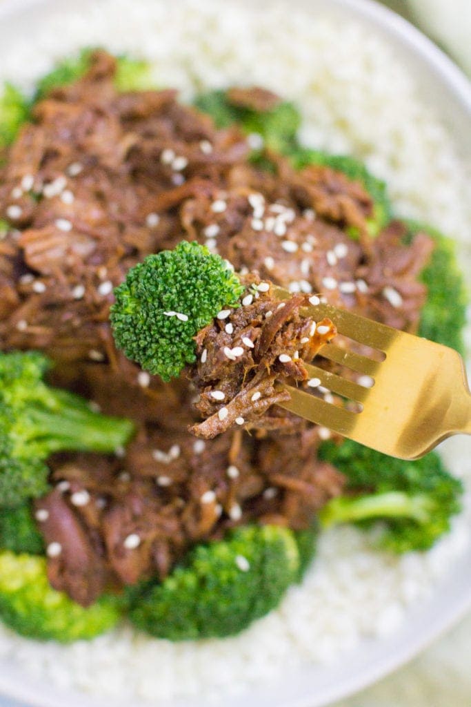 a bowl of Healthy Slow Cooker Beef and broccoli with a gold fork taking a bite out of it.